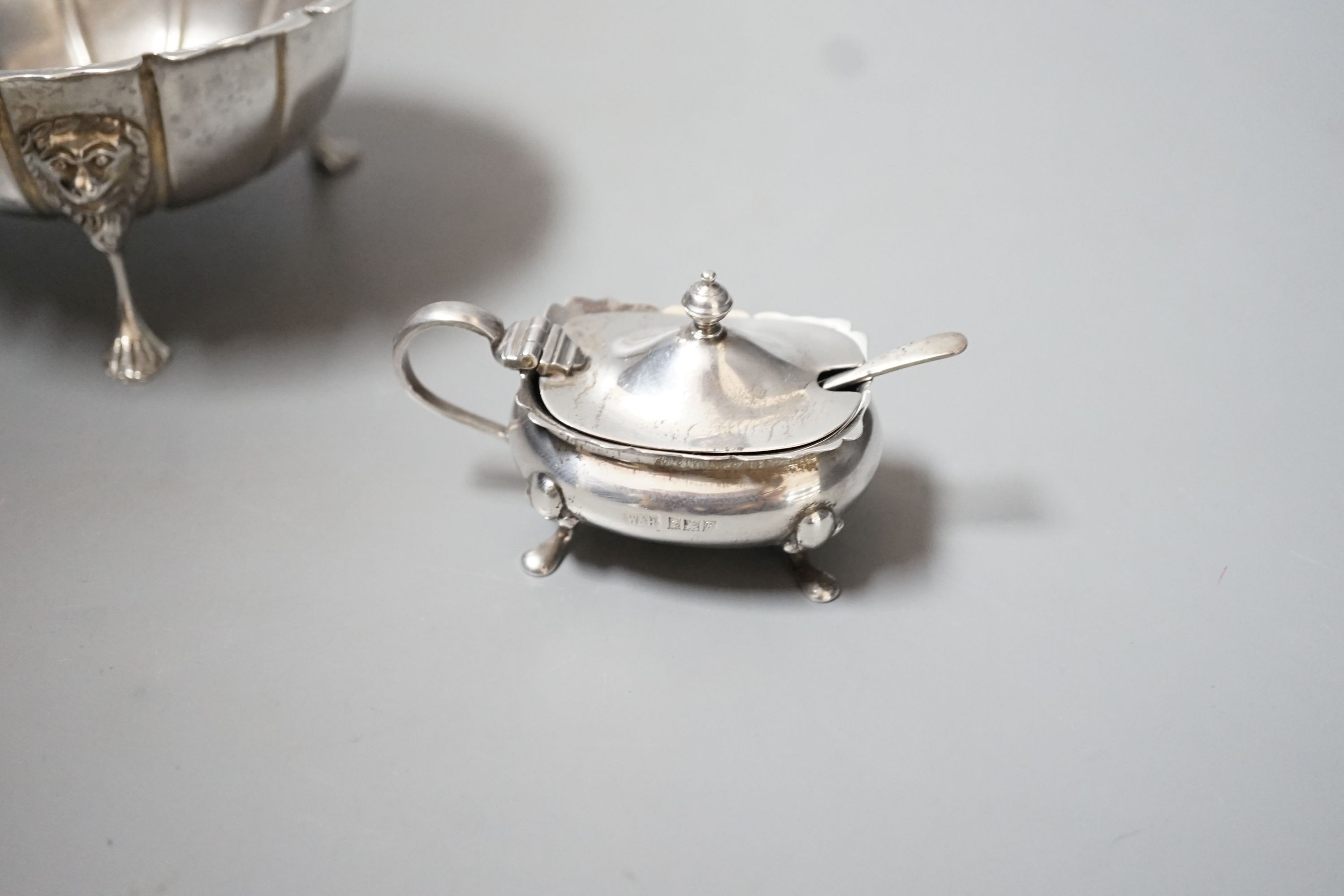 A George V Irish silver bowl, with lion mask knees on tripod supports, West & Son, Dublin, 1923, diameter 11.4cm and a silver mustard pot and spoon, 60z.